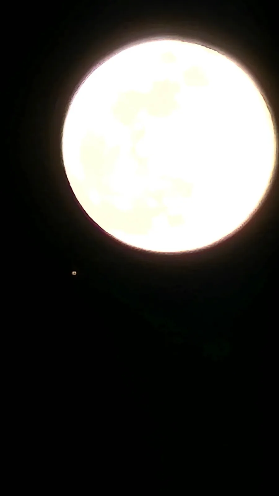 A bright, full moon dominates a dark night sky, viewed through a circular aperture. A small, distant, glowing object, likely…