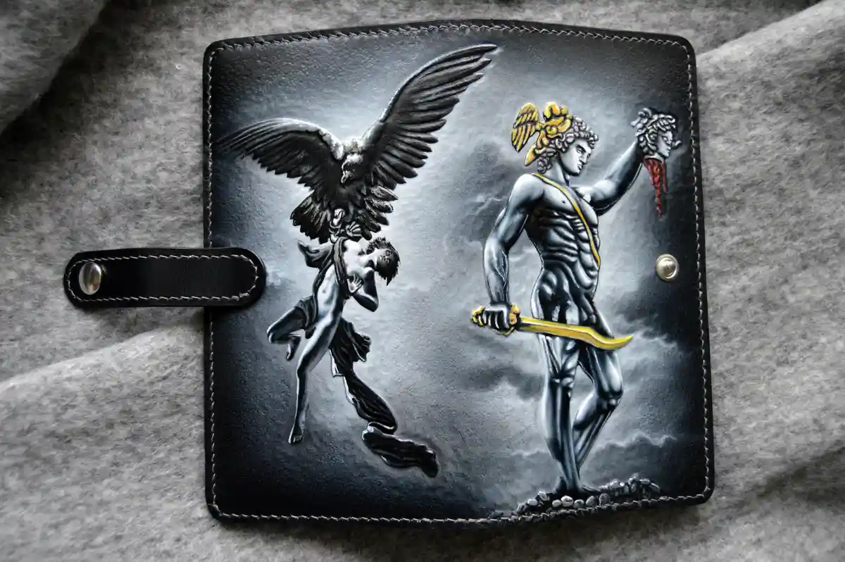 a black leather wallet with intricate hand-carved imagery depicts the mythological hero hercules holding the severed head of…