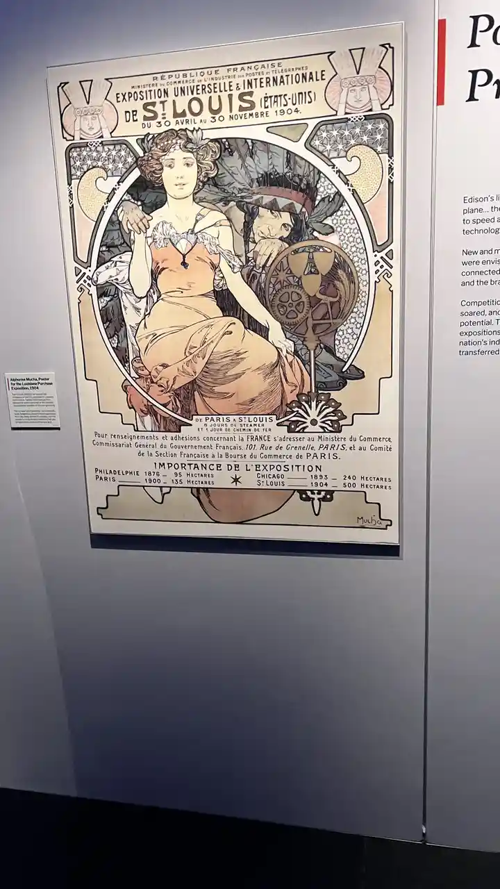 A vintage Art Nouveau poster by Alphonse Mucha, displayed in a museum, advertises the 1904 St. Louis World's Fair with…