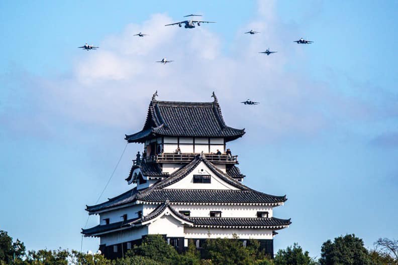 A traditional Japanese castle with white walls and dark tiled roofs stands under a blue sky with scattered clouds. Multiple…