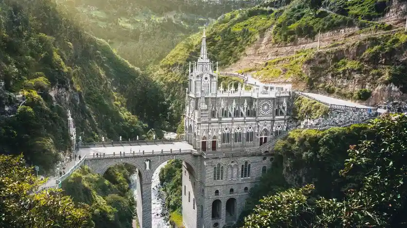 a stunning gothic-style church built into a mountainous canyon, featuring a tall spire, arched windows, and a stone bridge…
