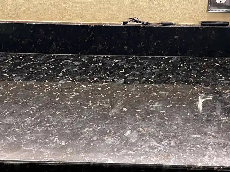 A close-up photo of a dark, speckled granite countertop with a black USB cable and a small black device resting on the edge…