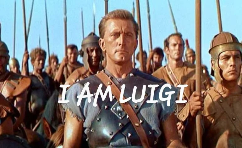 A still from a historical film shows a Roman soldier in armor standing in front of a line of other soldiers holding spears…