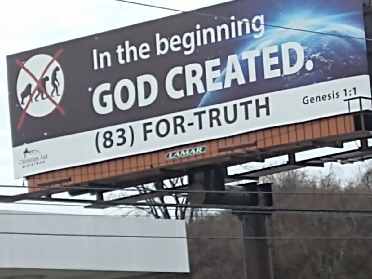 A billboard from Christian Aid Ministries displays the text 'In the beginning GOD CREATED.' with 'Genesis 1:1' cited, and…