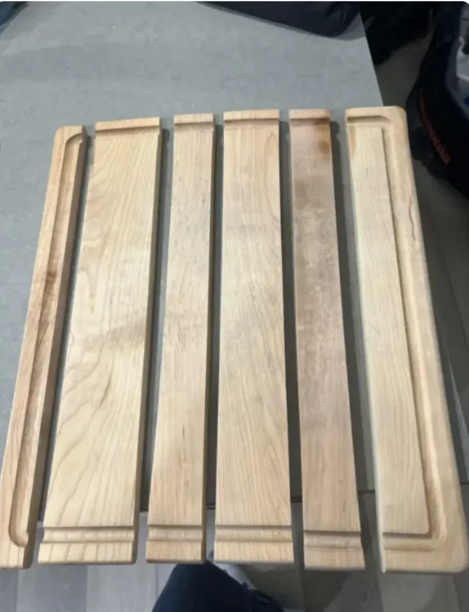 A top-down photo shows six light-colored wooden planks arranged side-by-side on a gray surface, forming a rectangular…