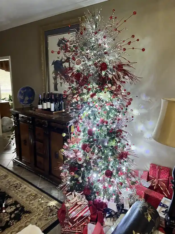 a heavily decorated christmas tree with red and silver ornaments, candy cane lights, and sparkly tinsel stands in a living…