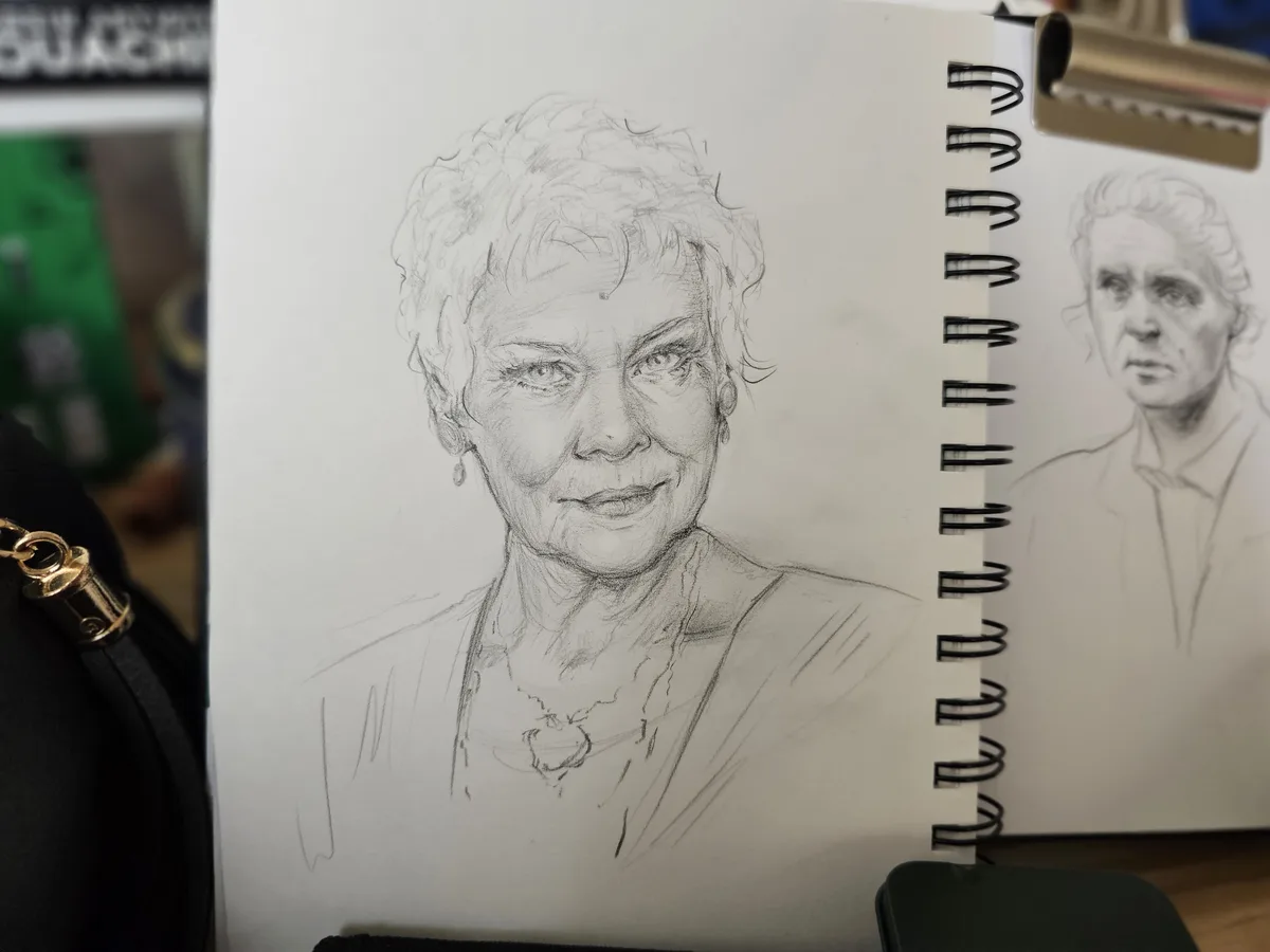 A sketchbook shows two pencil portraits of an older woman; the left page features a detailed, smiling portrait, while the…