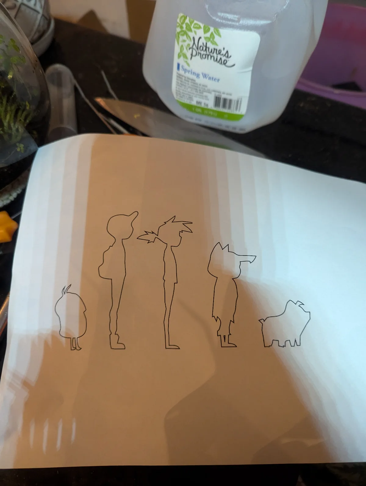 A hand-drawn sketch on paper shows five simple black outline figures resembling cartoon characters, including two taller…
