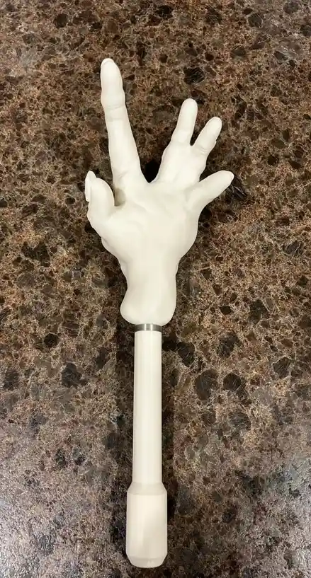 A white plastic hand prop, resembling a zombie or Halloween decoration, is attached to a long white handle and rests on a…