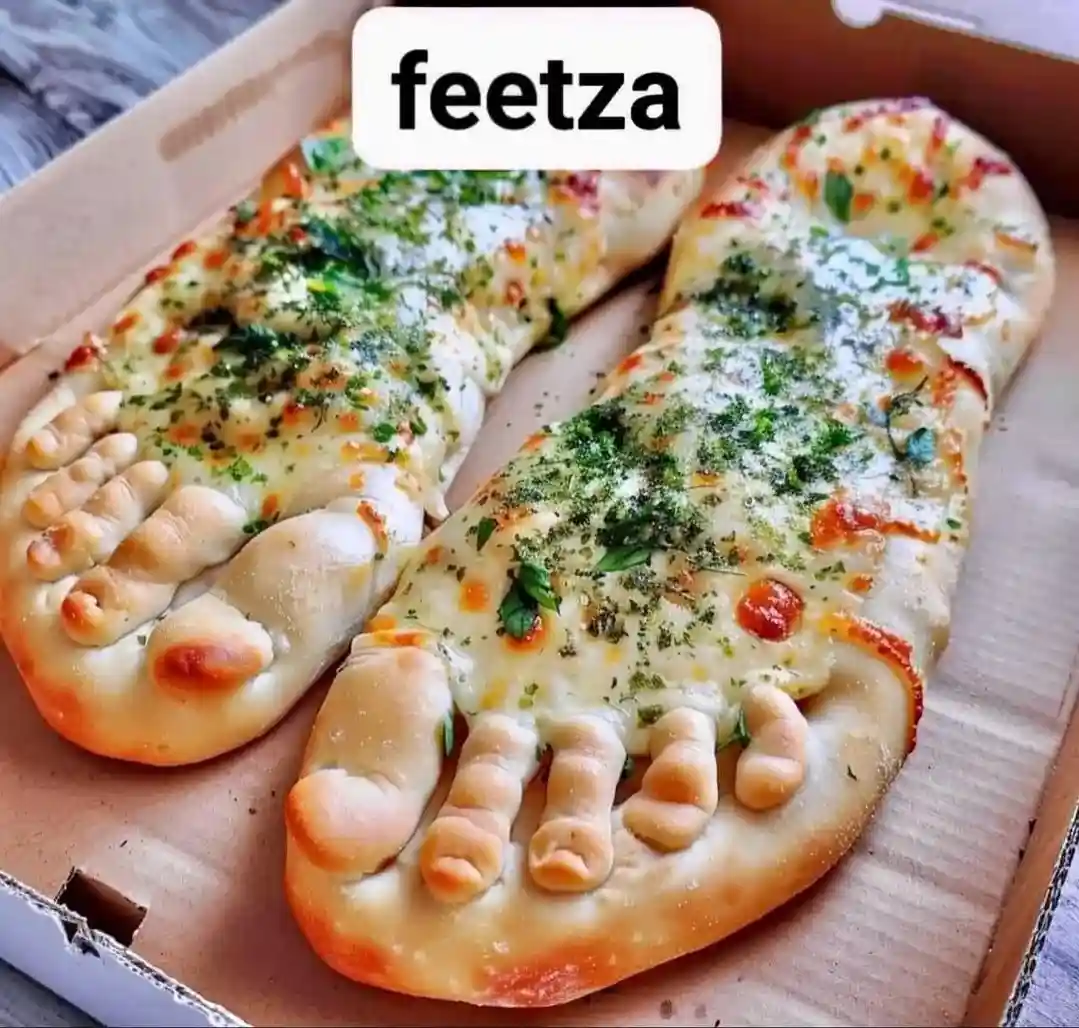 Two pizza slices shaped like human feet, complete with toes, are presented in a cardboard pizza box. They are topped with…