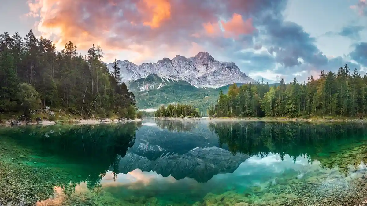 Standing astride the Austrian border, the 10,000-foot Zugspitze peak towers above serene Eibsee Lake, which perfectly…