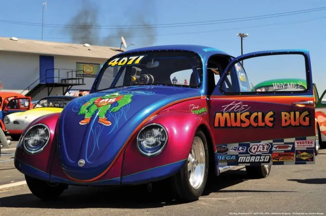 A heavily modified, colorful blue and purple Volkswagen Beetle race car with the name 'The Muscle Bug' painted on its side…