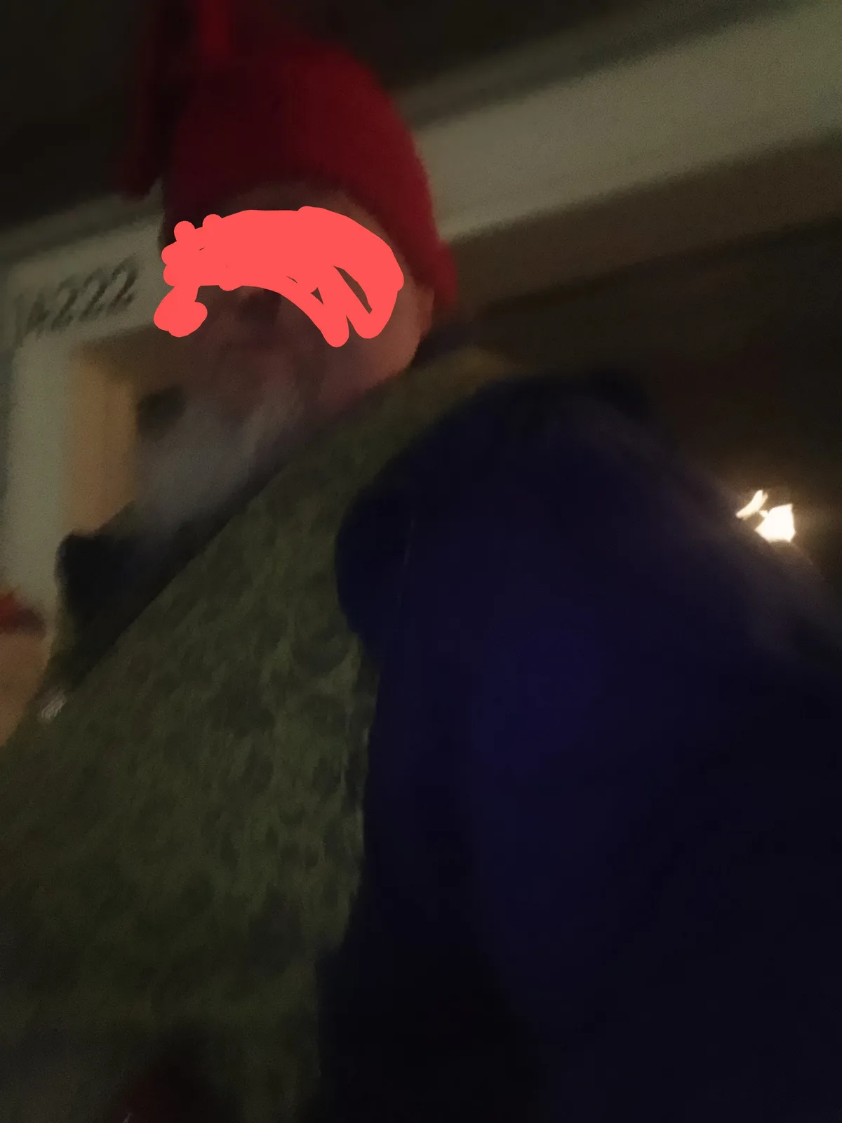 A blurry, low-light selfie shows a person wearing a red beanie and a dark jacket, with their face obscured by a red…