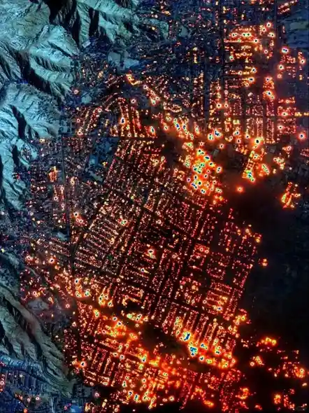 An aerial night view of a city nestled in mountains, with thousands of bright orange and red glowing points indicating…