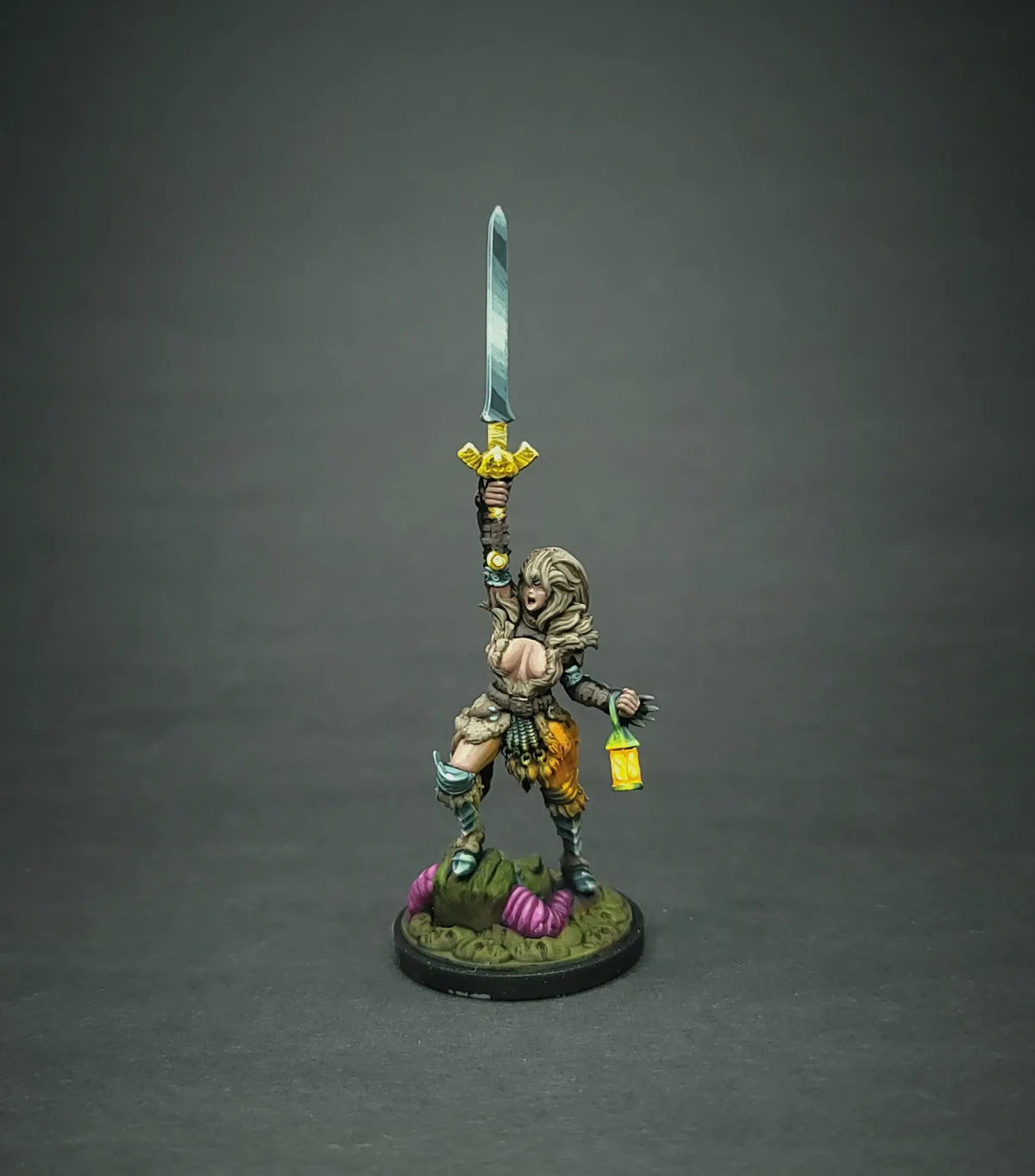 A painted fantasy miniature of a female warrior stands on a circular base, holding a large sword aloft in one hand and a…