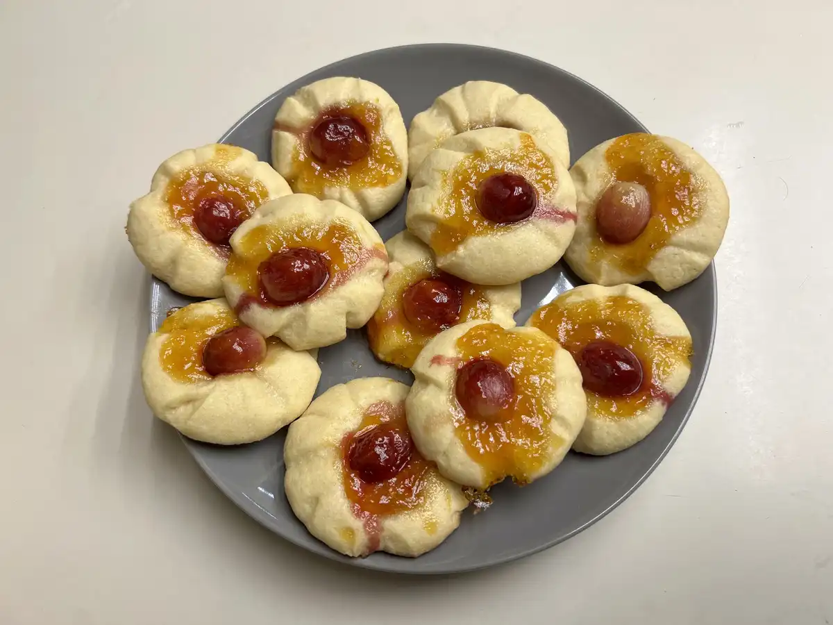 A gray plate holds several small, flower-shaped cookies with golden-brown edges, each topped with a glossy orange-yellow jam…