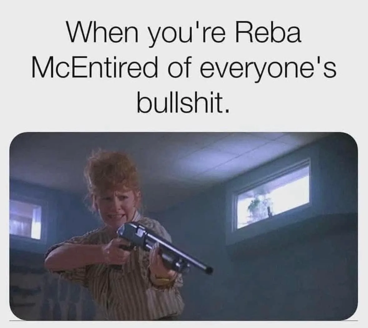 A woman with curly red hair, wearing a striped shirt, aims a shotgun directly at the viewer with a determined, slightly…
