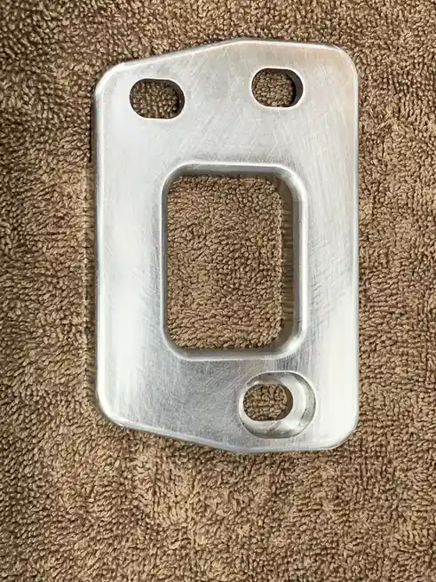 A brushed metal object with three holes and a rectangular cutout, resembling a phone case, rests on a brown textured towel…