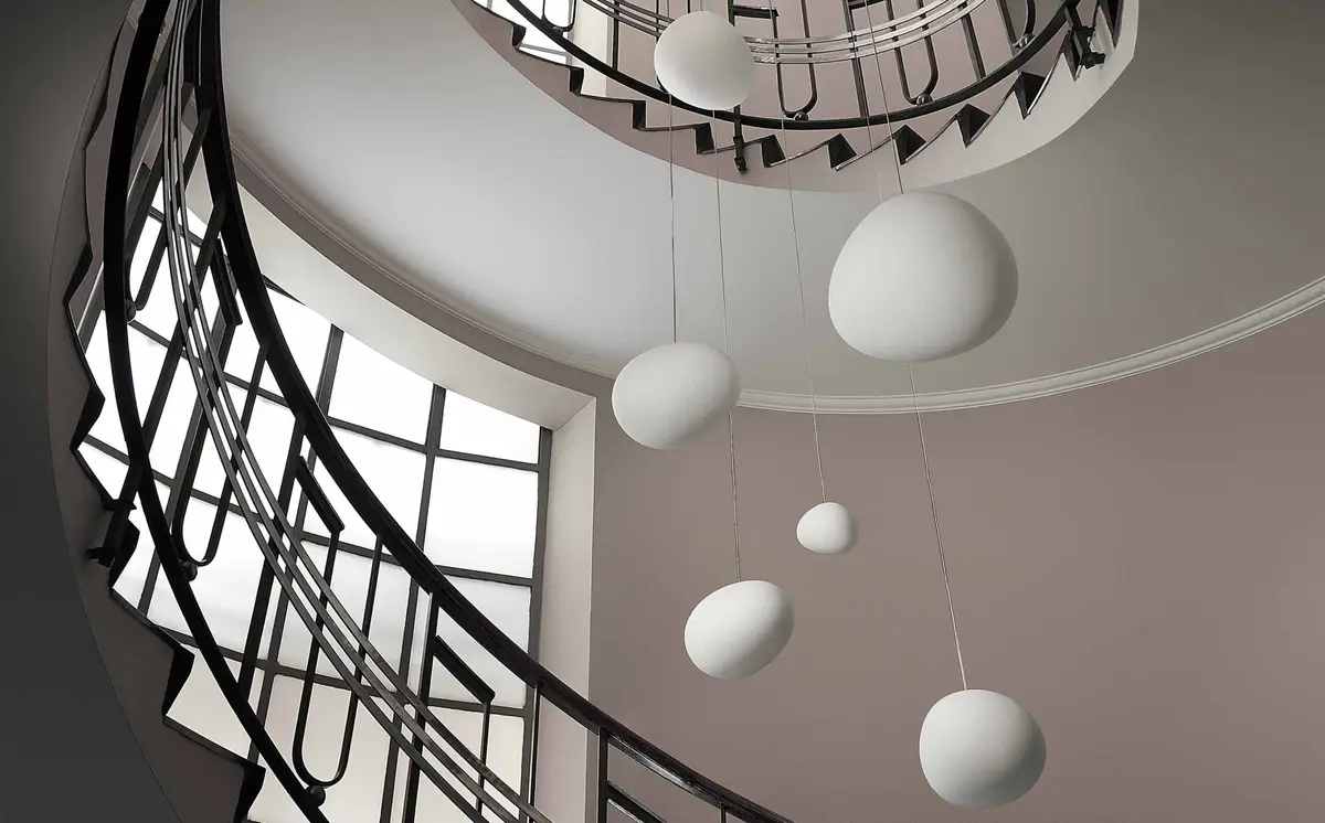 A low-angle shot of a spiral staircase with black metal railings and large windows, featuring several white, egg-shaped…