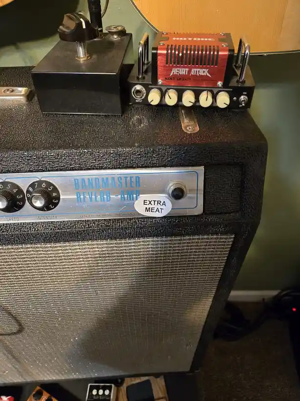 A close-up photo of a vintage Fender Bandmaster Reverb-Amp with a sticker reading 'EXTRA MEAT' on its control panel. On top…