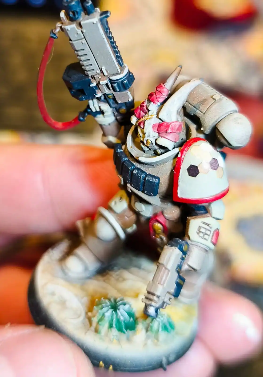 A close-up photo of a hand holding a painted miniature figurine of a heavily armored warrior with a helmet, holding a large…