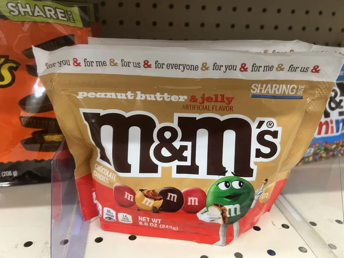 A close-up photo of a peanut butter & jelly flavored M&M's bag on a store shelf, featuring the brand's logo and a green M&M…
