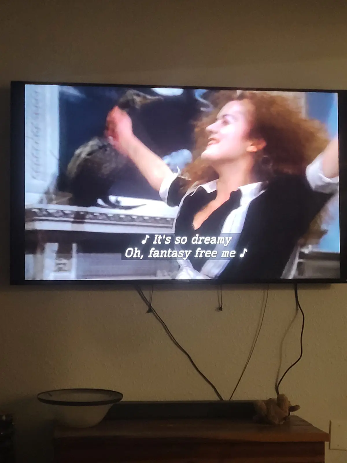 A television screen displays a scene from a movie or show featuring a woman with curly red hair, wearing a black and white…