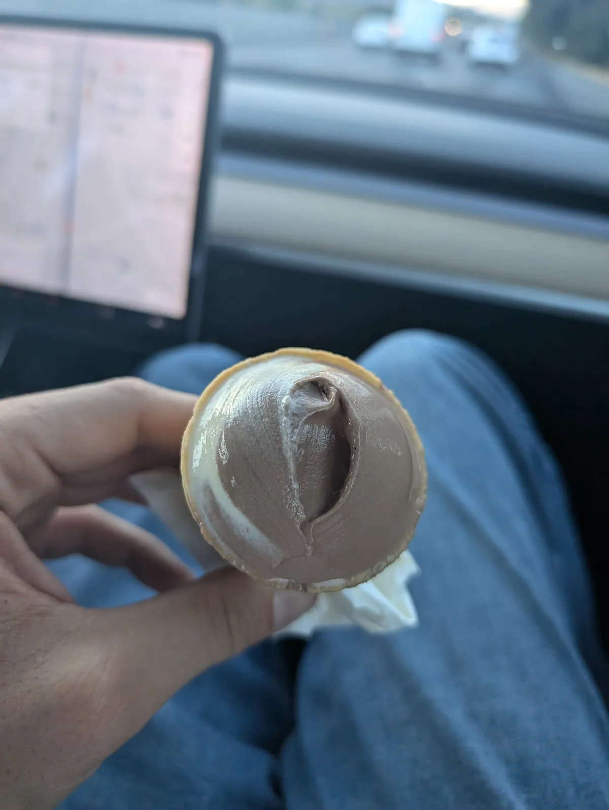 A hand holds a chocolate ice cream cone upside down, revealing the ice cream has been scooped out to resemble a phallic…