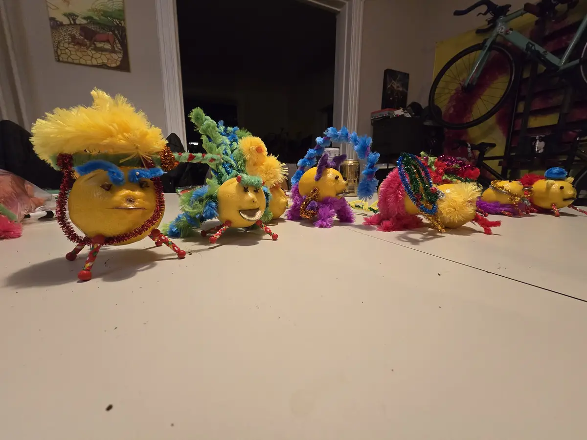 A row of lemons decorated with colorful pom-poms, pipe cleaners, and glittery accessories to look like dancing characters…