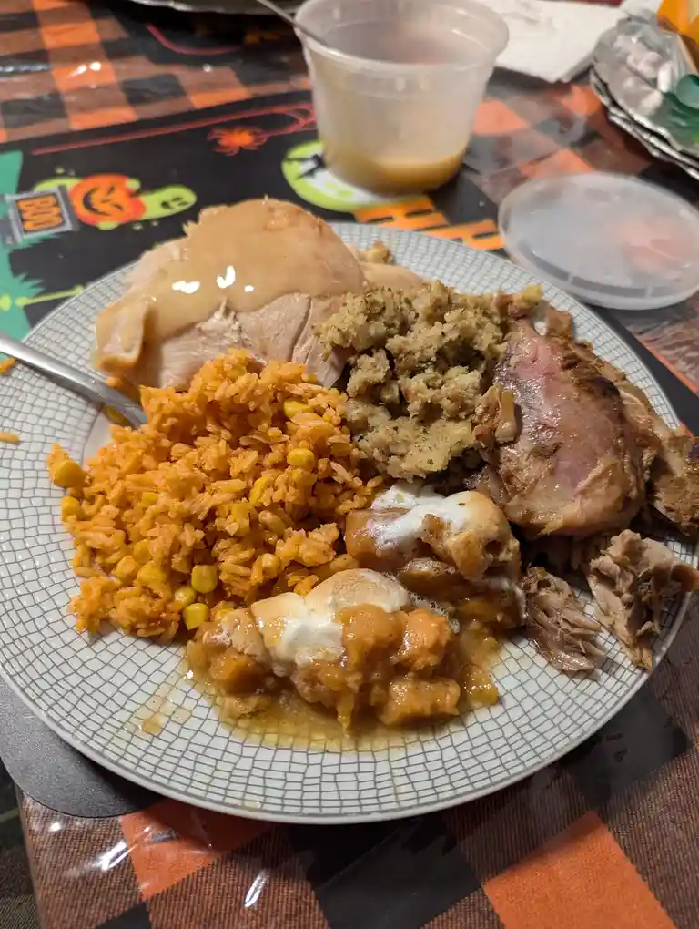 A plate of Thanksgiving-style food including turkey, stuffing, orange rice with corn, and sweet potato casserole with…