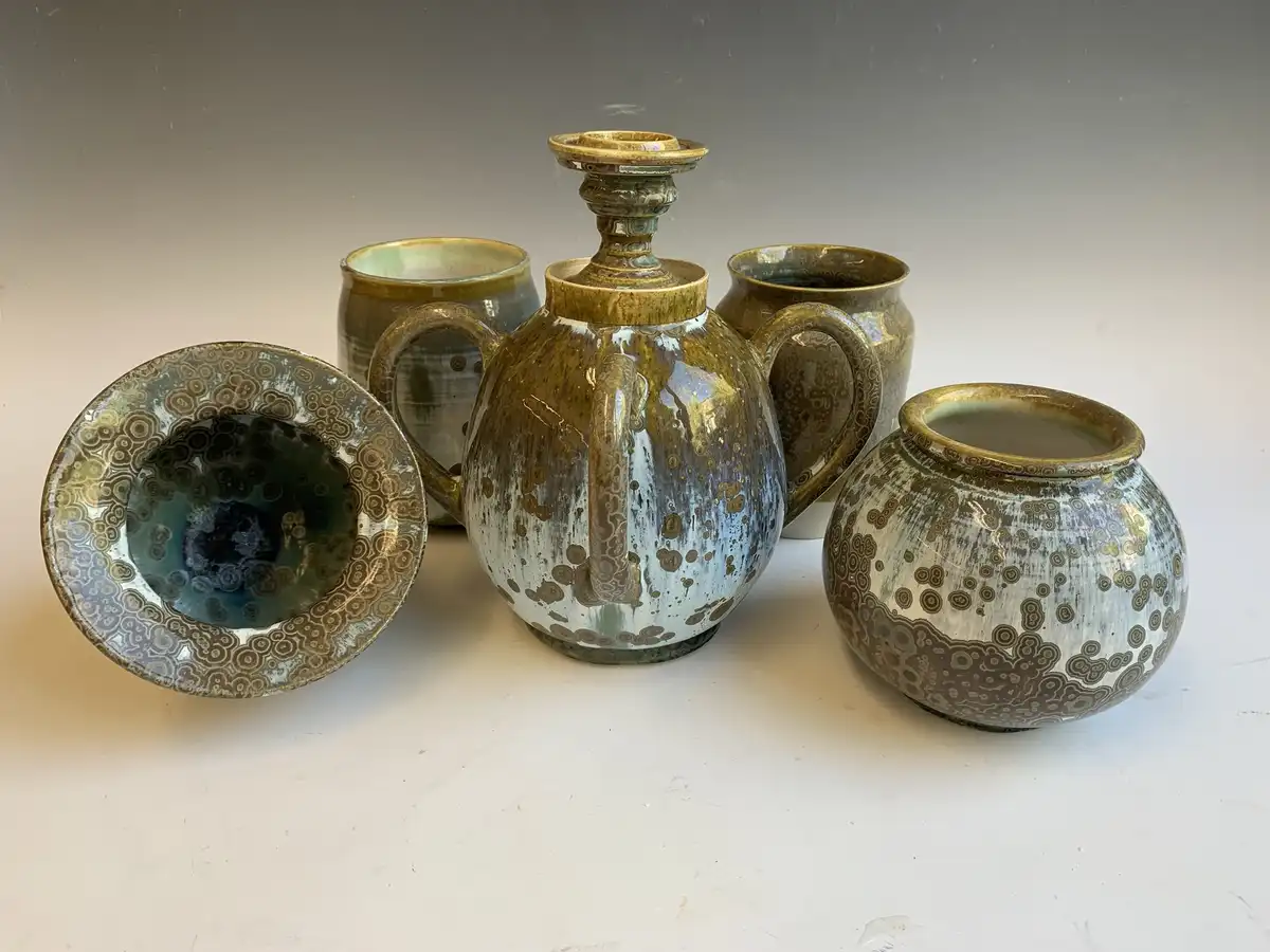 A collection of handmade ceramic pottery, including a central decanter with two handles and a lid, surrounded by four other…