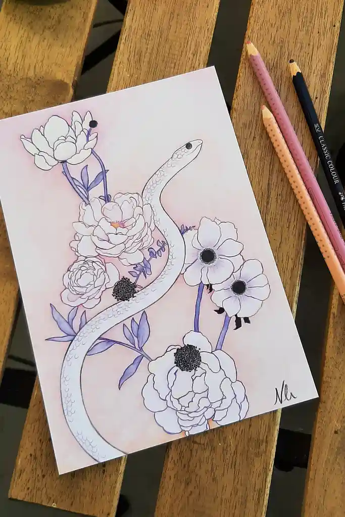 A colored pencil drawing on paper shows a white snake coiled among white and light purple flowers, including peonies and…