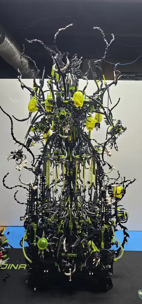 a towering, intricate lego sculpture resembling a monstrous, biomechanical tree with black and neon yellow pieces, featuring…