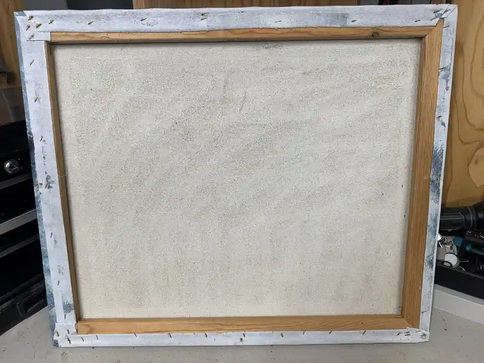 The image shows the back of a large, rectangular canvas with a wooden frame and a white fabric backing, leaning against a…
