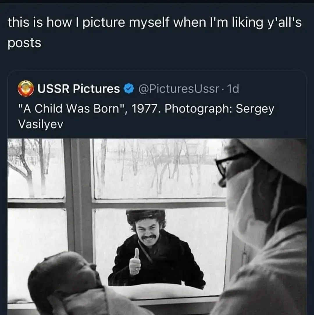A black-and-white photo shows a man with a mustache giving a thumbs-up through a window while a nurse holds a newborn baby…