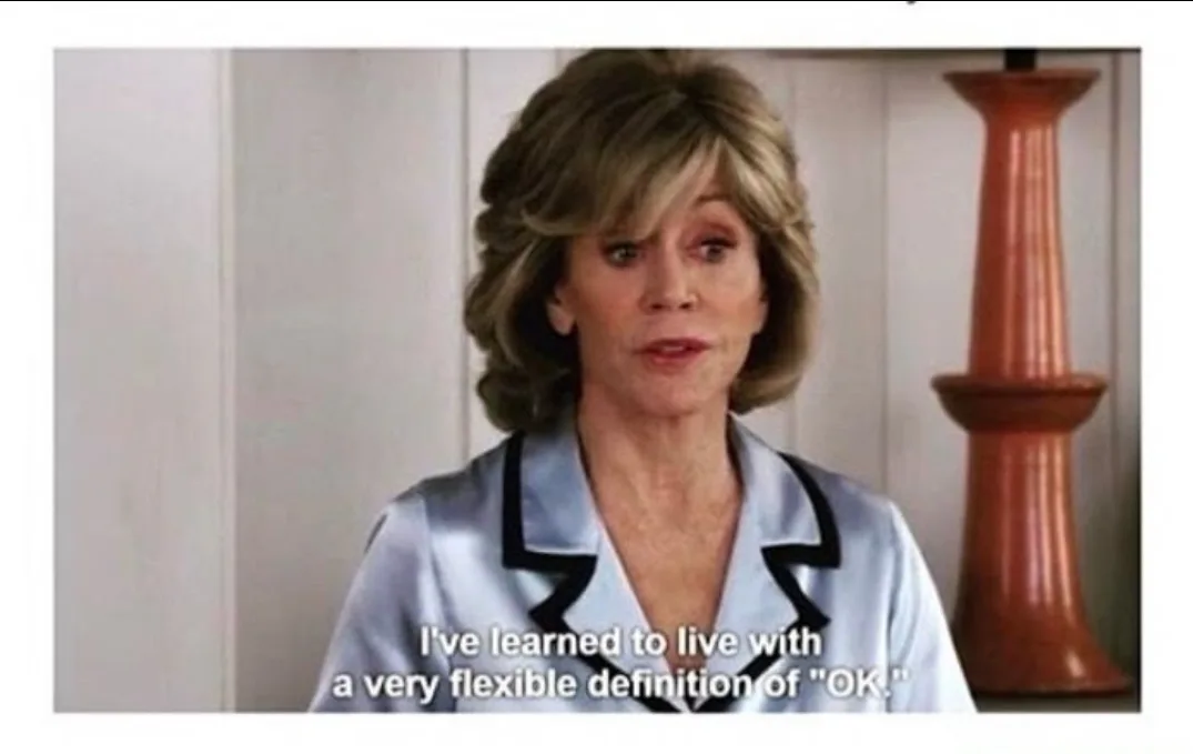 A woman with short, styled blonde hair wearing a light blue satin pajama top with black trim looks directly at the camera…