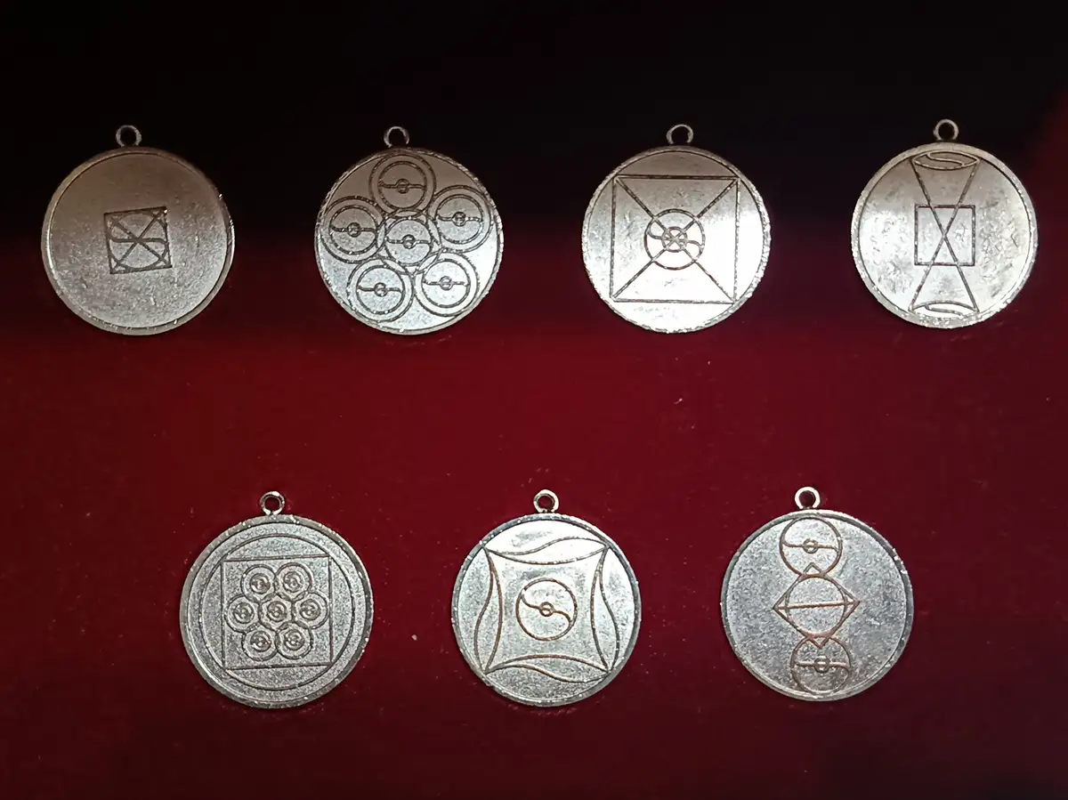 Seven silver circular pendants with various geometric and symbolic engravings are arranged in two rows on a dark red velvet…