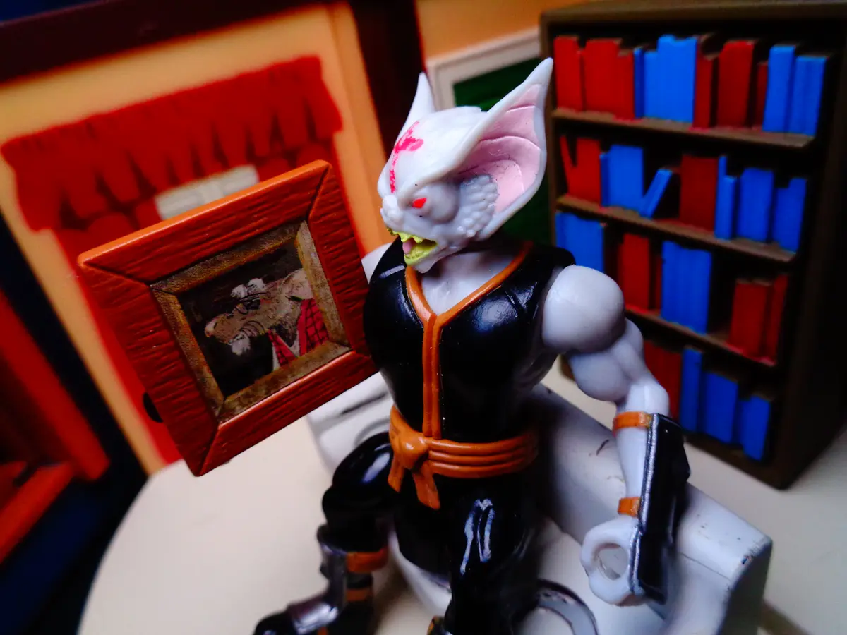 A white-furred, muscular anthropomorphic cat figurine with red eyes and a bloodstain on its forehead stands in a room with…