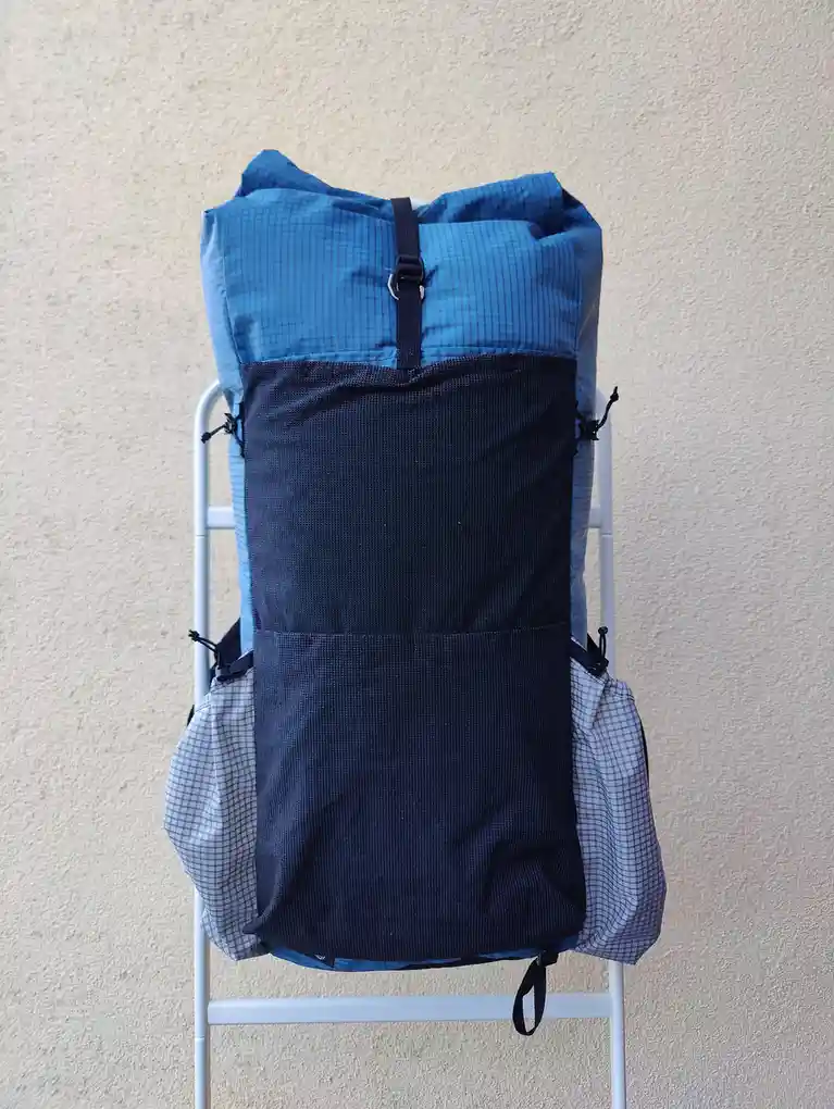 A blue and black backpack with a checkered pattern is stuffed with clothes and sits upright on a white metal ladder against…