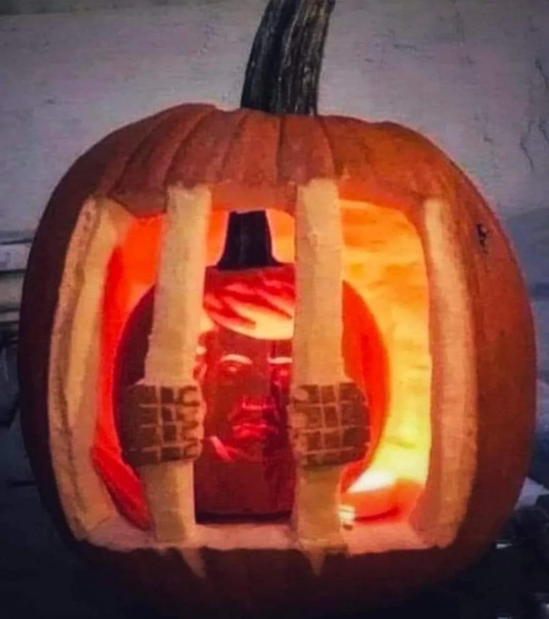 A carved pumpkin with a glowing interior features a detailed face of a man with a mustache and hat, framed by two vertical…