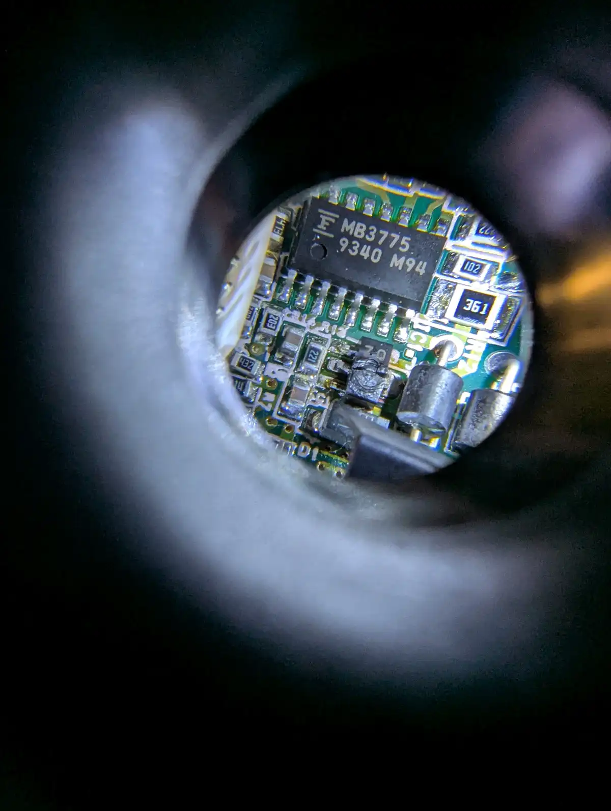 A close-up view through a magnifying lens shows a small green circuit board with various electronic components, including a…