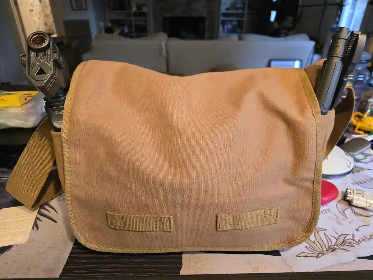 A tan canvas messenger bag sits on a table, with two toy blasters (one resembling a lightsaber hilt) sticking out of its…