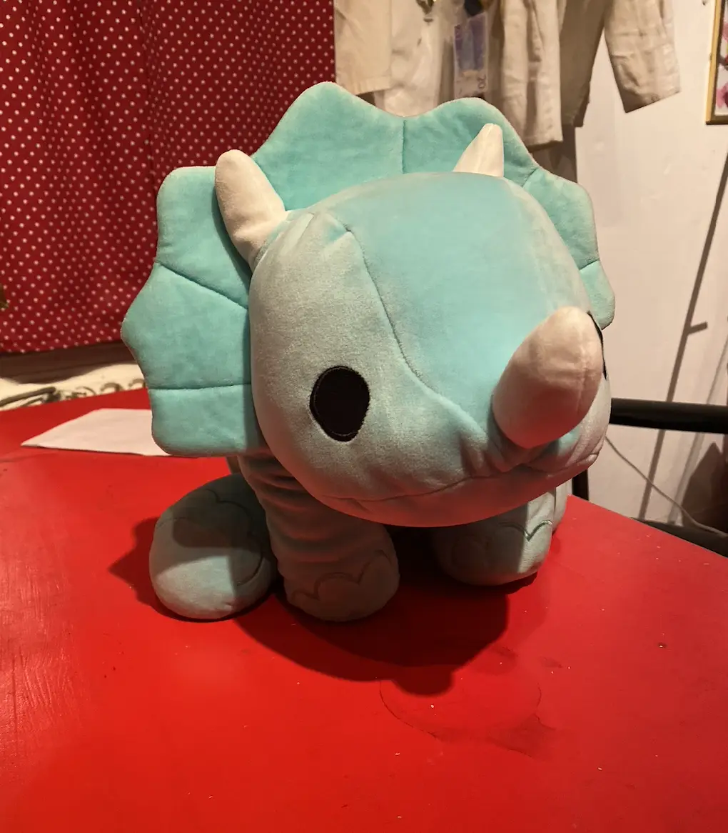 A light blue plush toy resembling a triceratops with a single, prominent rhino-like horn on its snout, sitting on a red…