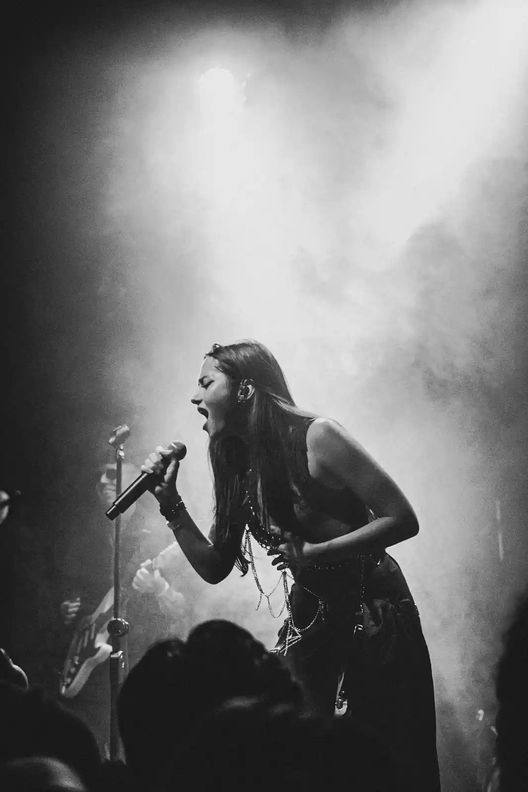 A black and white photo of a female singer passionately performing on stage, holding a microphone, with stage lights and…
