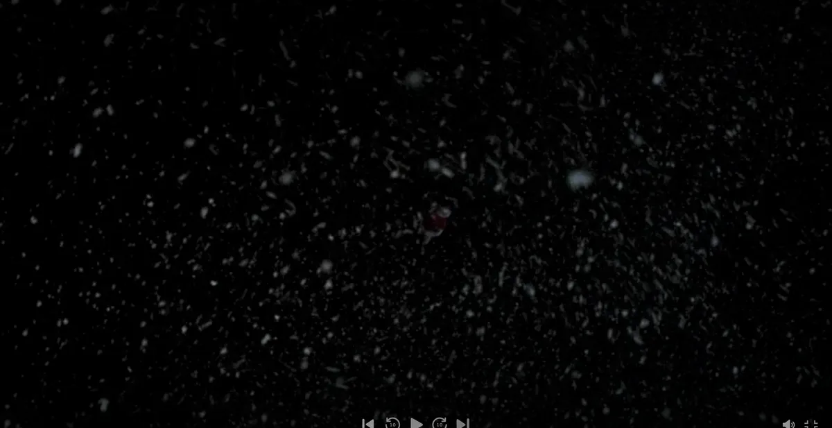 A dark, snowy scene shows a tiny, blurry figure in red and white, resembling Santa Claus, surrounded by falling snowflakes…