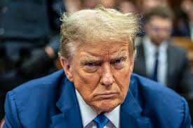 a close-up photo of Donald Trump with a stern, unimpressed facial expression, wearing a blue suit and tie, looking slightly…