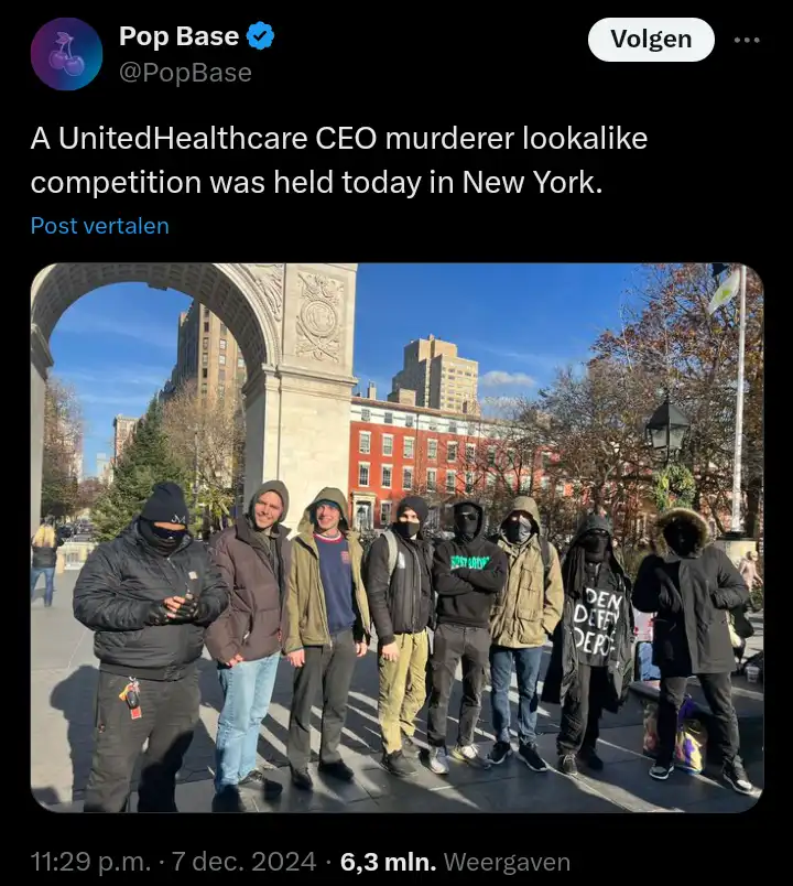 A group of seven men posing outdoors under a large stone archway, likely in New York City, with some wearing hoodies and…