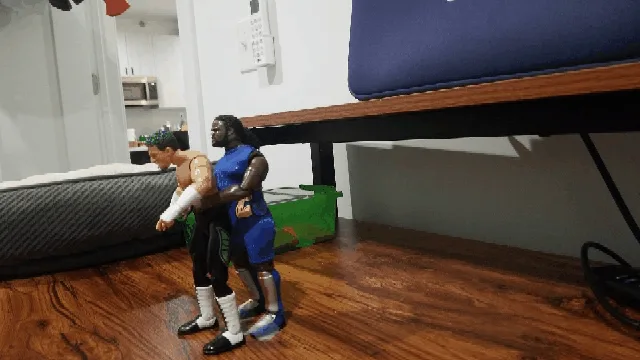 A sequence of six images shows two wrestling action figures under a bed, starting with one figure lifting the other, then…