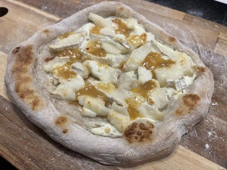 A freshly baked, rustic pizza with a puffy, flour-dusted crust sits on a wooden cutting board. The pizza is topped with…