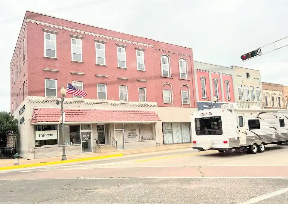 A street view of a small town with a red brick building housing a Thrivent Financial office, an American flag flying, and a…